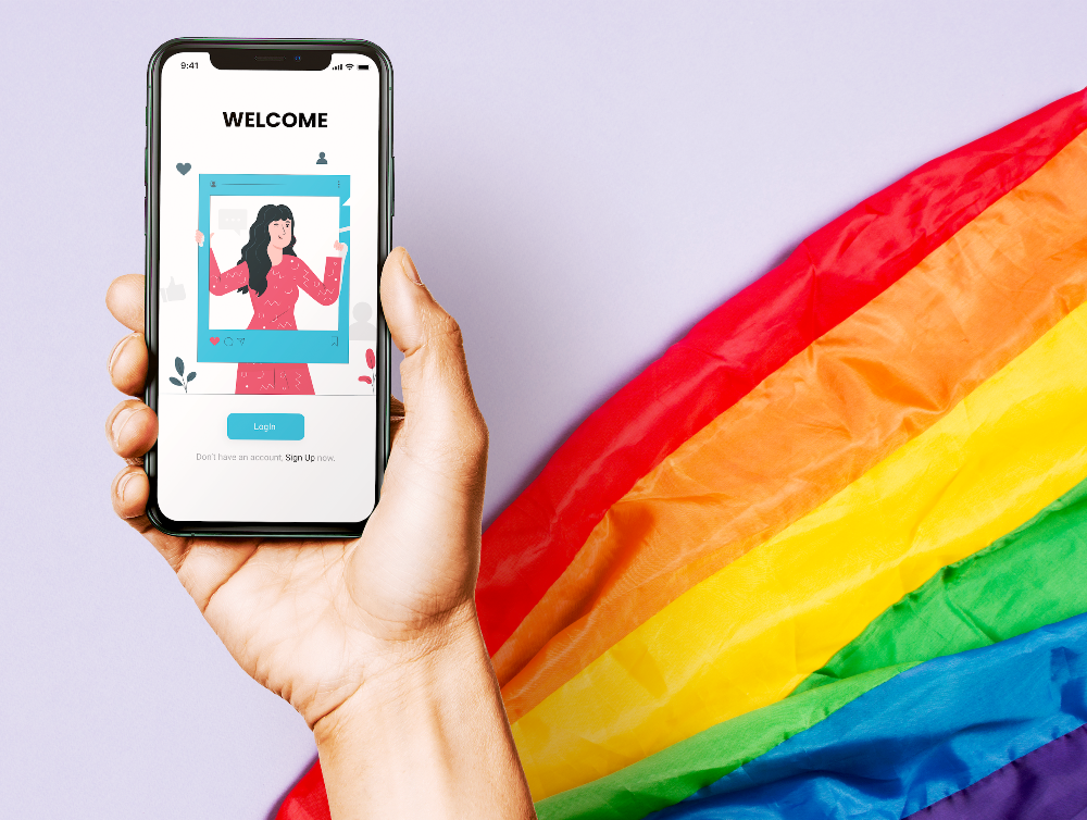 Hand holding a phone with the study app welcome screen, in front of a rainbow flag
